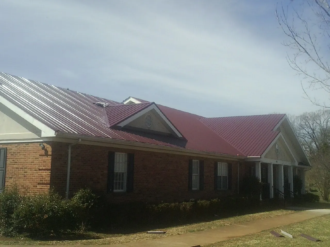 Red metal roof with gabled entries on a long brick building, from a Hail Damage Roof Repair job in Stoneville
