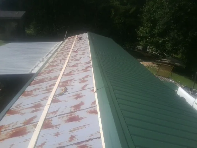 Old rusted panels beside newly installed green metal roofing — Wind Damage Roof Repair by Roofing Brothers in Stoneville