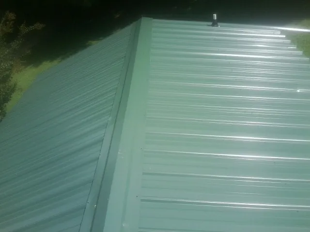 New green metal panels meeting at the ridge of a roof — Flat Roof Repair work by our crew in Stoneville