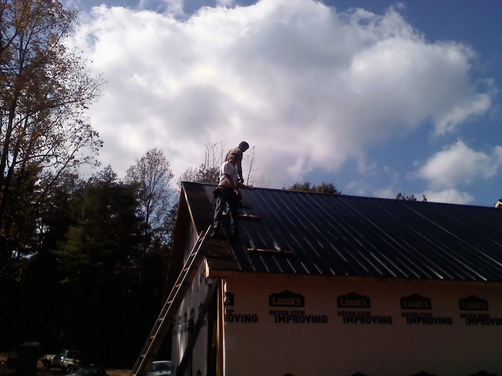 Roofer fastening dark metal panels high against a cloudy sky, from a Roof Inspection job in Stoneville