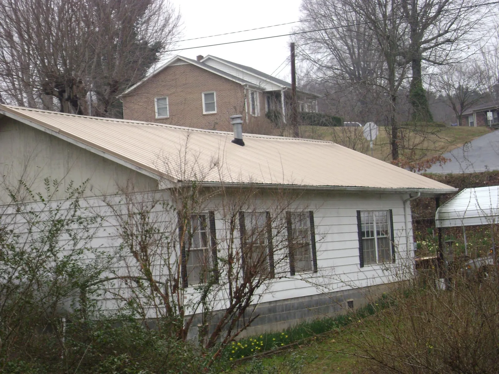Tan metal roof on a white sided house set into a hillside — Commercial Roofing by Roofing Brothers in Stoneville