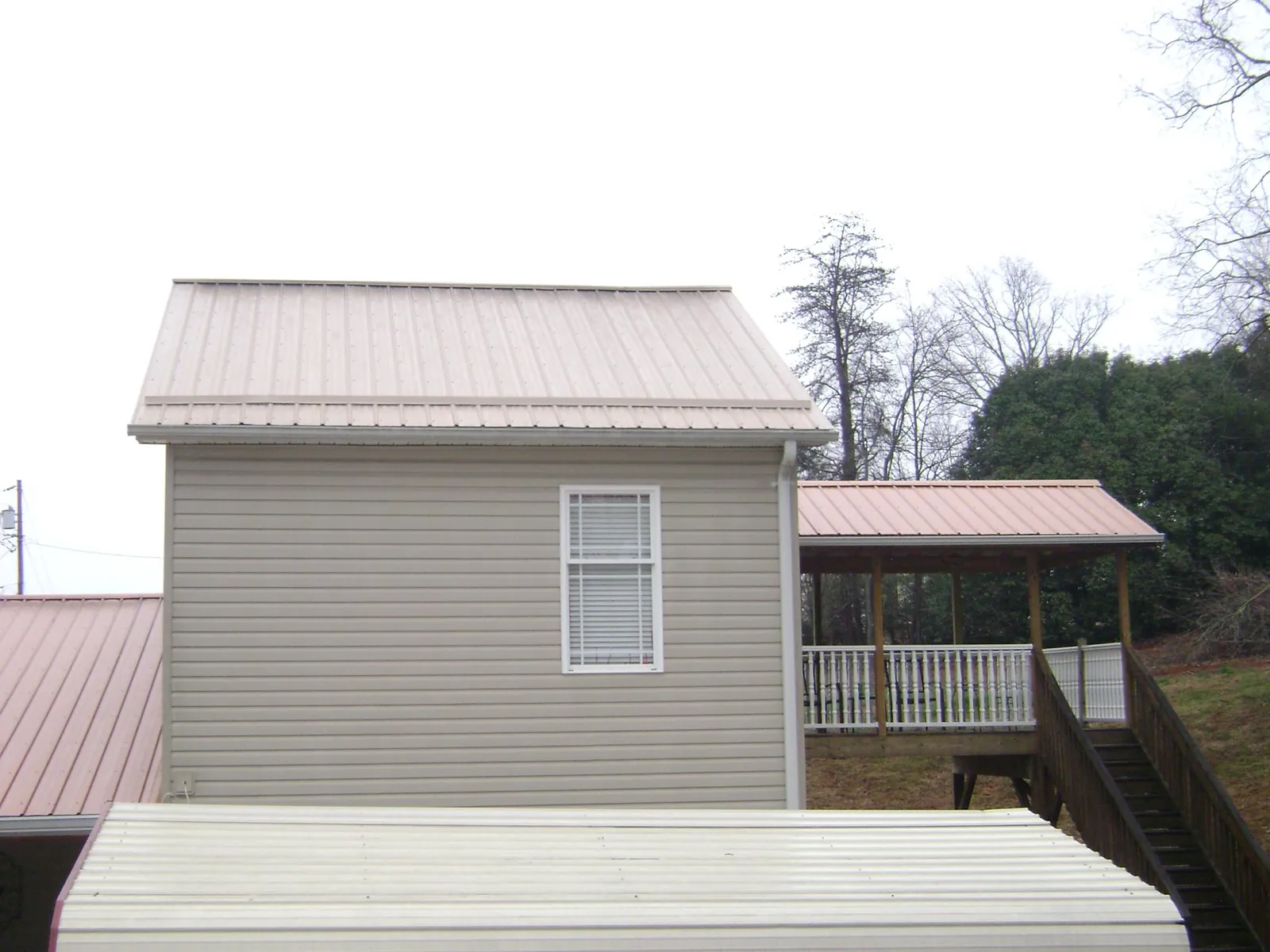 Tan metal roofs on a two story addition and attached porch, from a Roof Replacement job in Stoneville